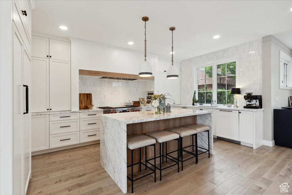 Kitchen with a center island, backsplash, light wood-style floors, a breakfast bar, and white cabinets