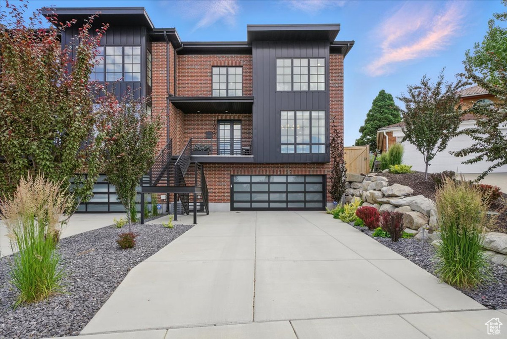 View of front of property with stairway, concrete driveway, an attached garage, and brick siding
