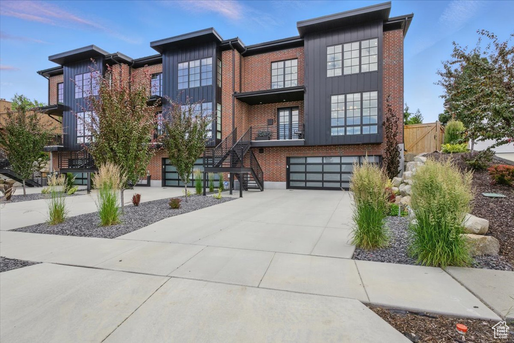 Contemporary home with stairway, concrete driveway, a garage, and brick siding