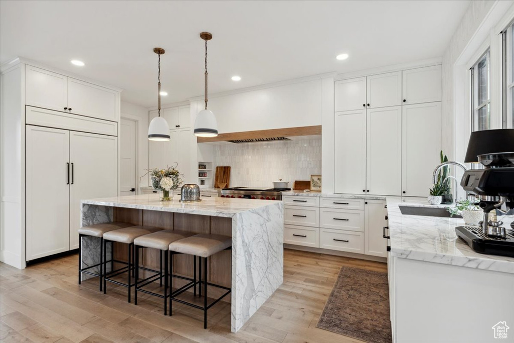 Kitchen with a kitchen island, light wood-type flooring, tasteful backsplash, light stone countertops, and recessed lighting