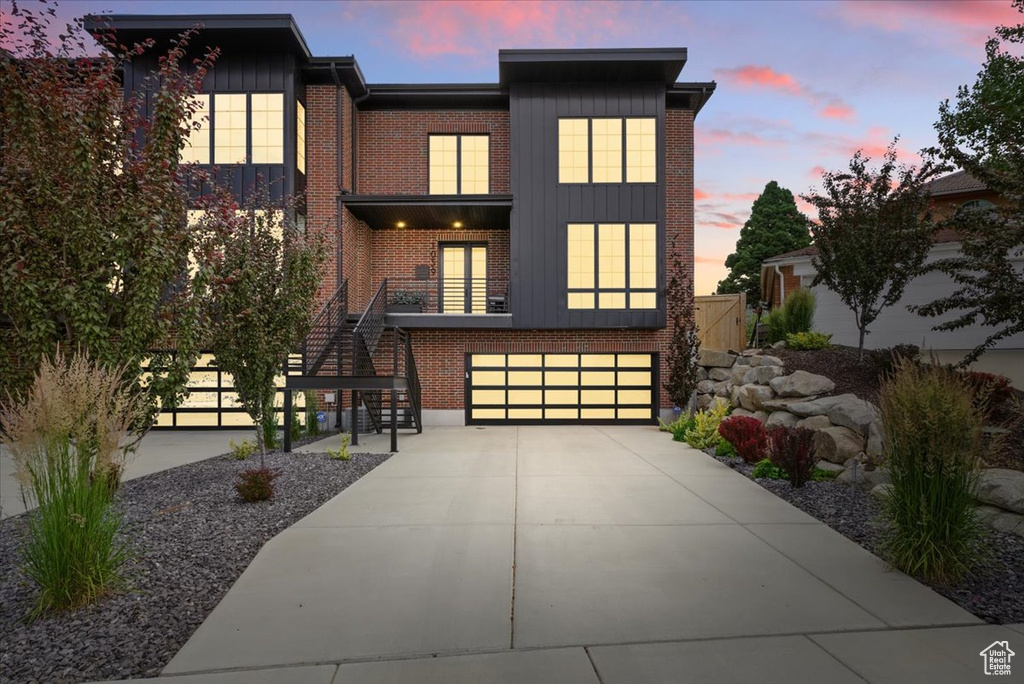 View of front facade with stairs, driveway, brick siding, an attached garage, and board and batten siding