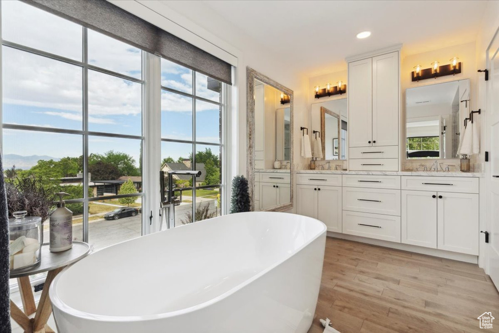 Bathroom with a freestanding tub, double vanity, wood finished floors, and recessed lighting