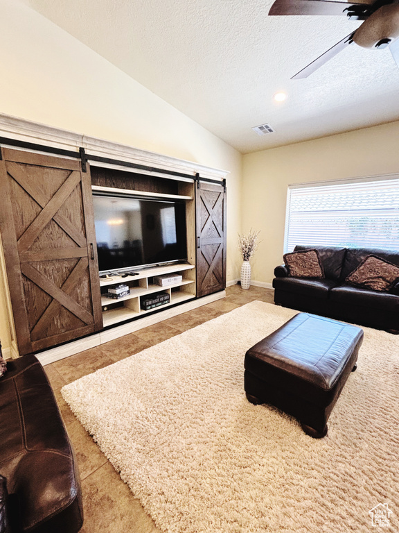 Tiled living area with a barn door, ceiling fan, vaulted ceiling, and a textured ceiling