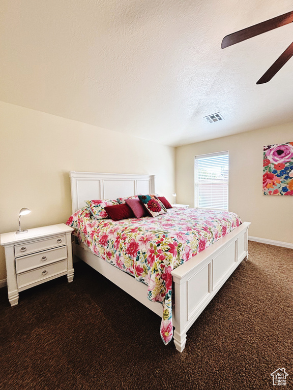 Bedroom with dark colored carpet, a textured ceiling, and ceiling fan