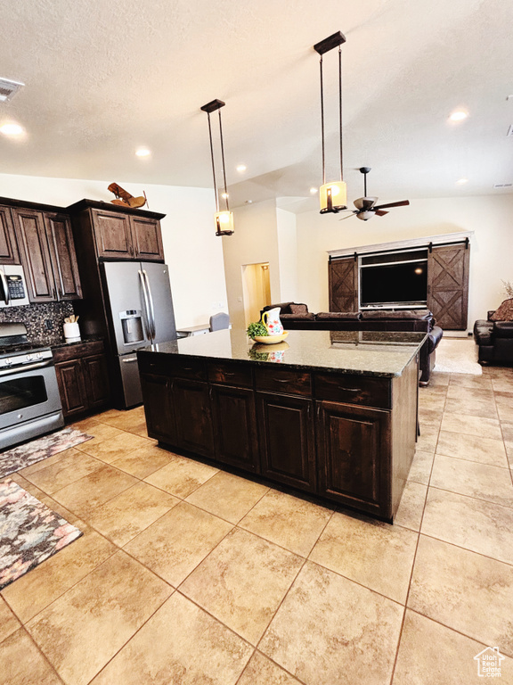 Kitchen with appliances with stainless steel finishes, open floor plan, a kitchen island, a ceiling fan, and decorative light fixtures