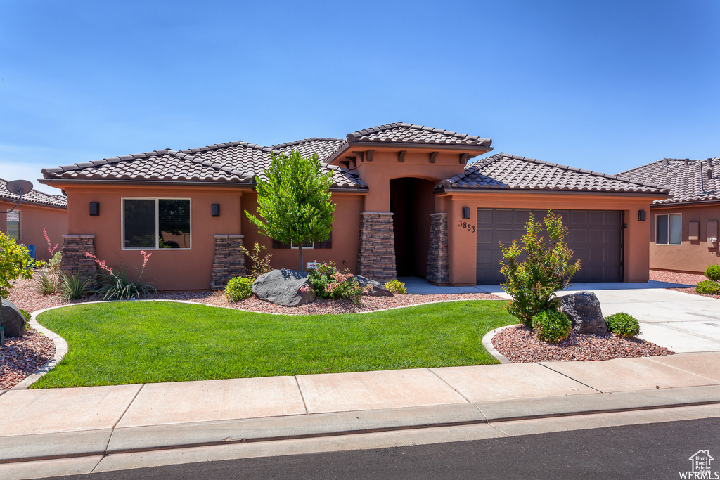 Mediterranean / spanish-style home with stucco siding, an attached garage, a front lawn, a tile roof, and driveway