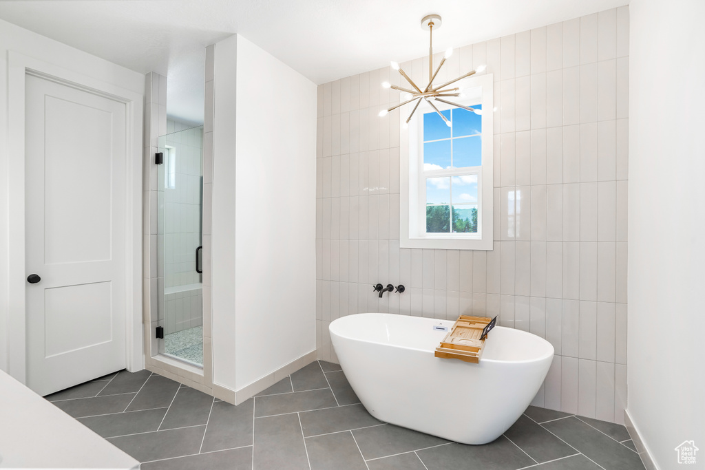 Full bathroom featuring tile walls, a chandelier, a freestanding tub, tile patterned flooring, and a stall shower