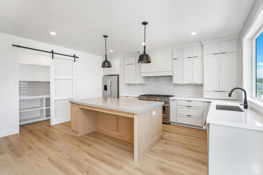 Kitchen featuring high quality appliances, tasteful backsplash, light wood-style floors, a barn door, and recessed lighting