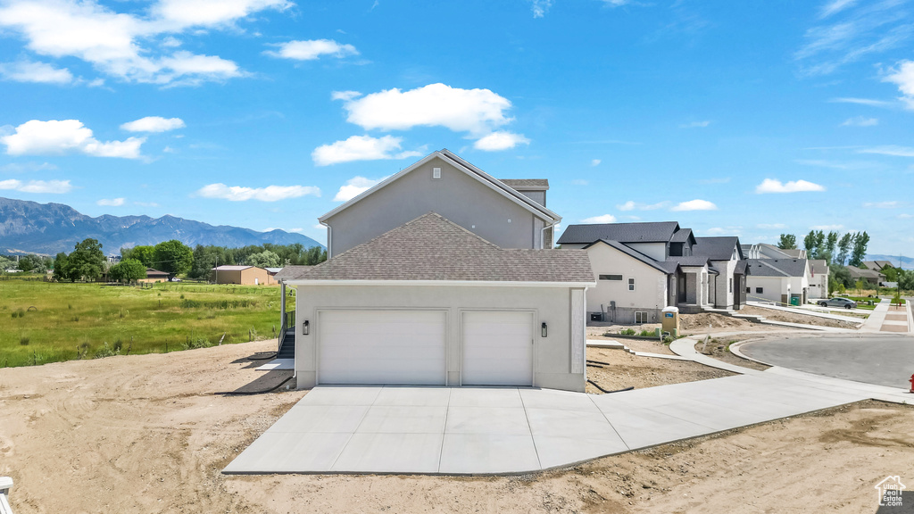 View of property exterior featuring stucco siding, an attached garage, concrete driveway, a mountain view, and a residential view