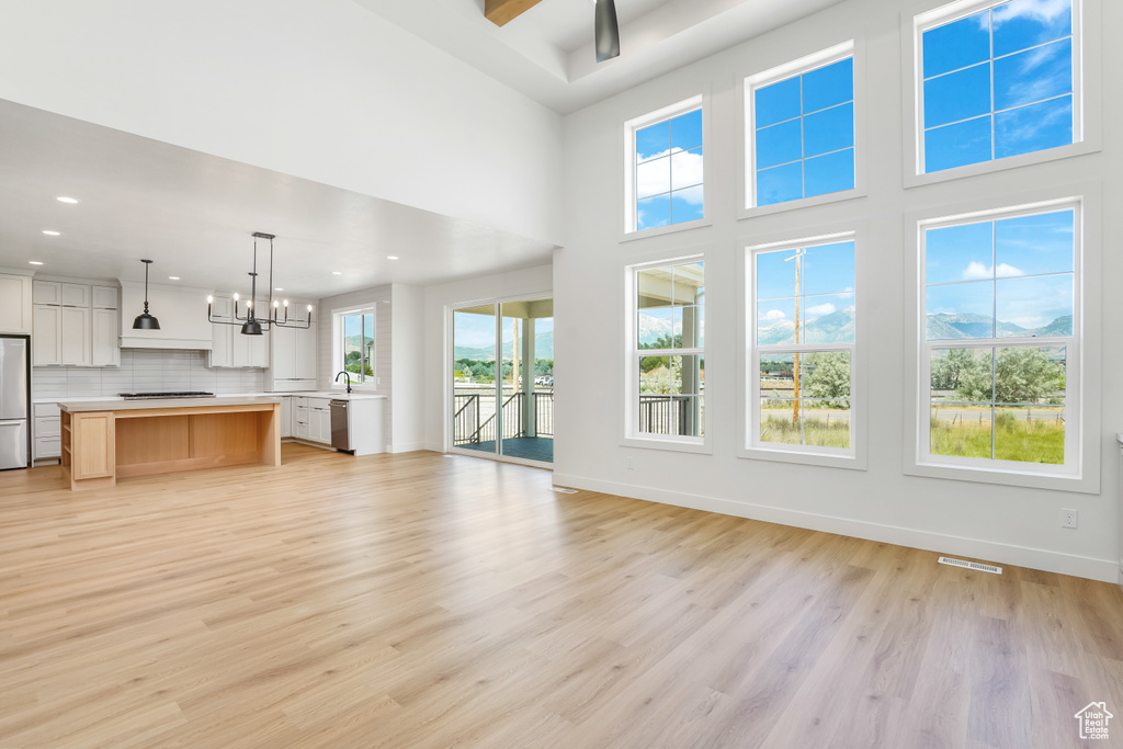 Unfurnished living room featuring a chandelier, light wood finished floors, recessed lighting, and a towering ceiling