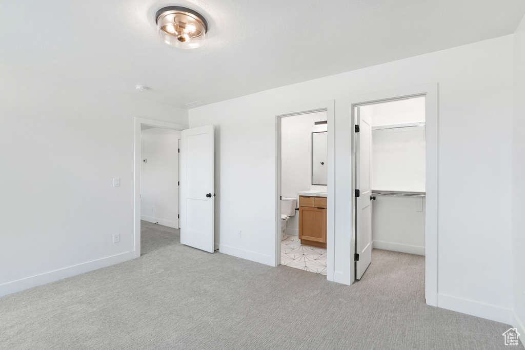 Unfurnished bedroom with light colored carpet, a walk in closet, connected bathroom, and a closet