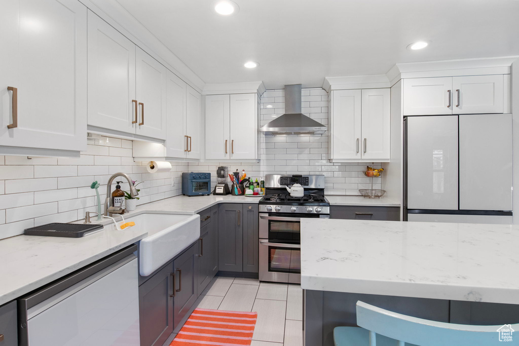 Kitchen with range with two ovens, wall chimney range hood, freestanding refrigerator, dishwasher, and light tile patterned flooring