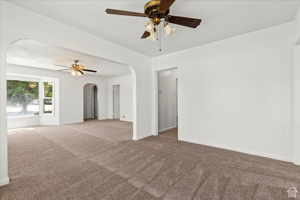 Carpeted empty room featuring ceiling fan and arched walkways