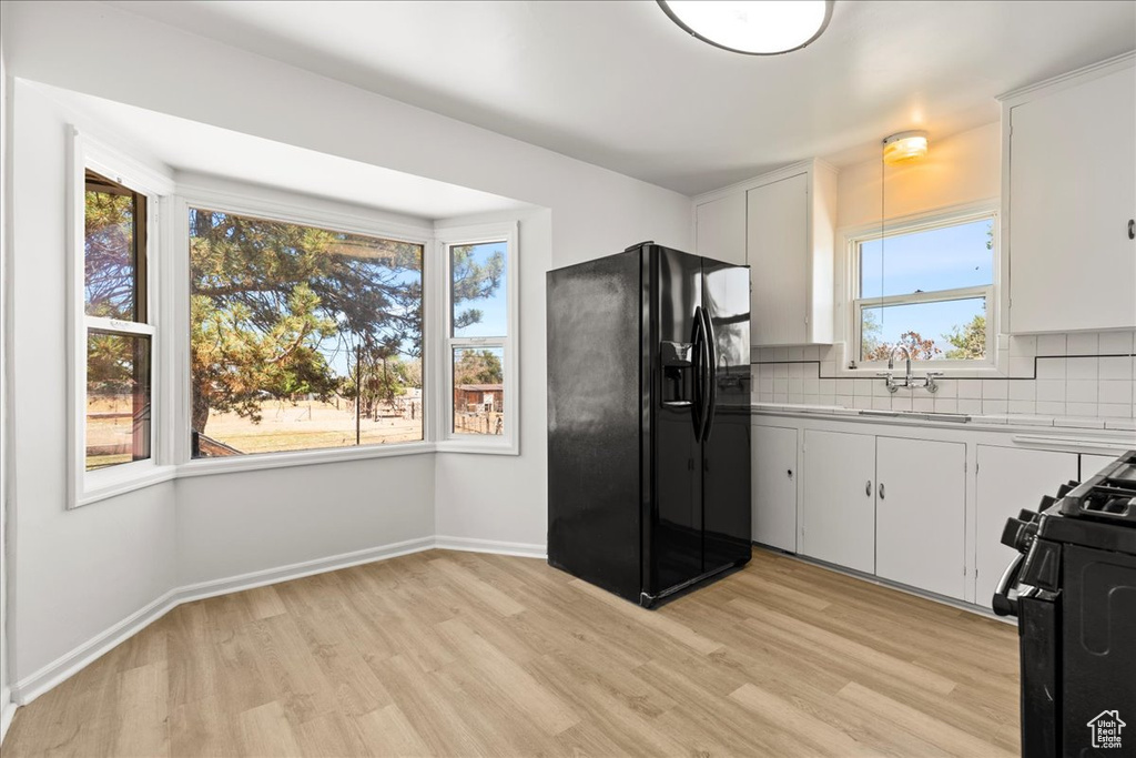 Kitchen featuring black appliances, light wood finished floors, tasteful backsplash, light countertops, and white cabinetry