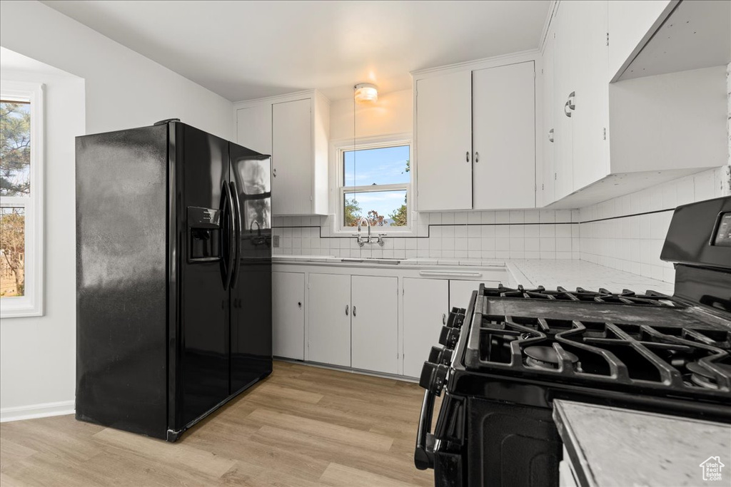 Kitchen featuring black refrigerator with ice dispenser, gas range, light countertops, light wood finished floors, and white cabinets