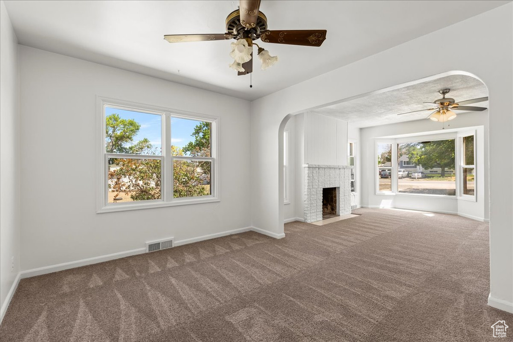 Unfurnished living room featuring carpet flooring, healthy amount of natural light, ceiling fan, and a brick fireplace