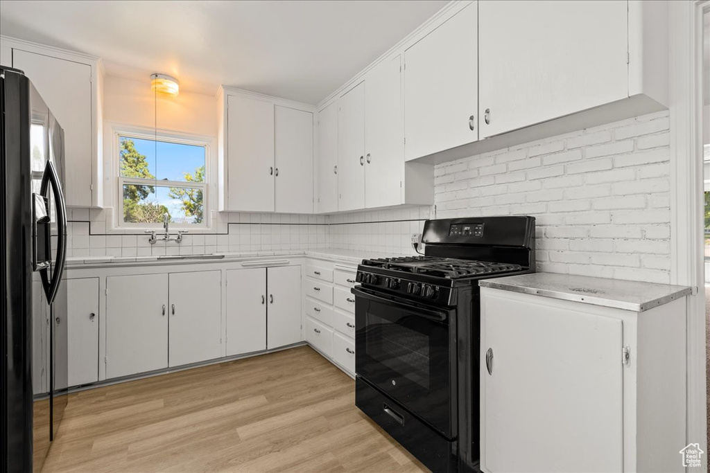 Kitchen with black range with gas cooktop, refrigerator with ice dispenser, white cabinets, and backsplash