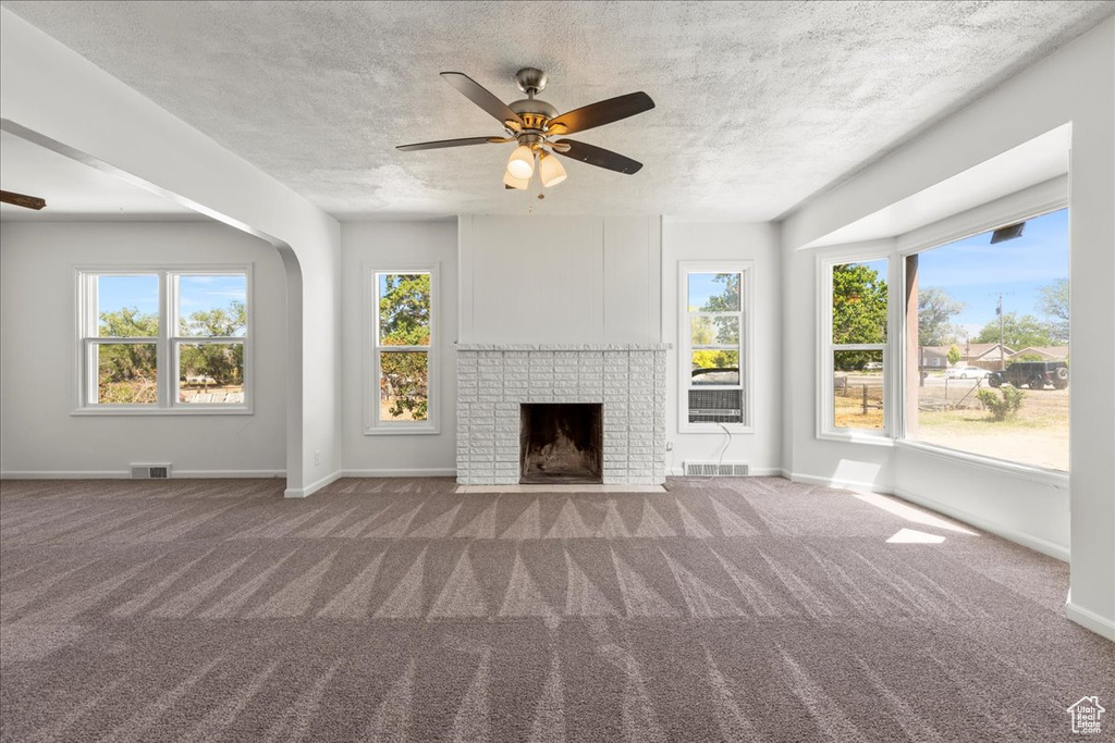Unfurnished living room featuring a ceiling fan, carpet, a fireplace, plenty of natural light, and a textured ceiling