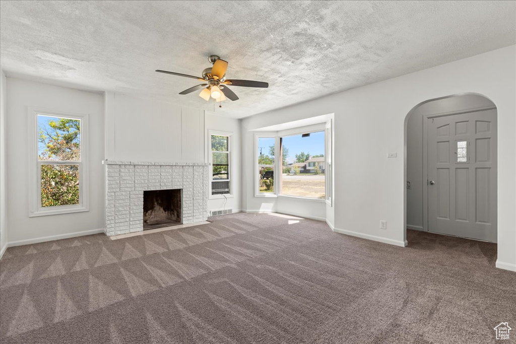 Unfurnished living room with carpet flooring, arched walkways, ceiling fan, a fireplace, and a textured ceiling