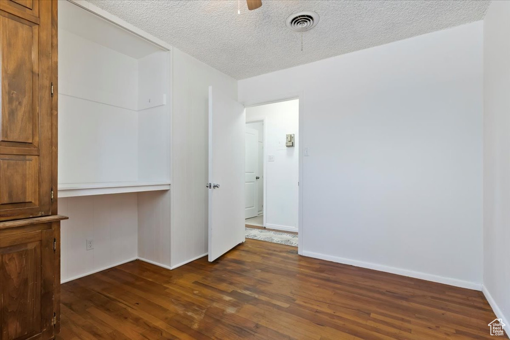 Spare room with dark wood-type flooring, a textured ceiling, a ceiling fan, and built in desk