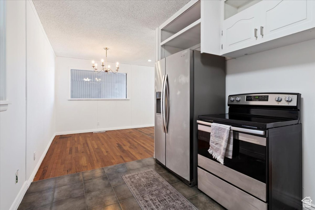 Kitchen with stainless steel appliances, a chandelier, white cabinetry, a textured ceiling, and dark tile patterned flooring