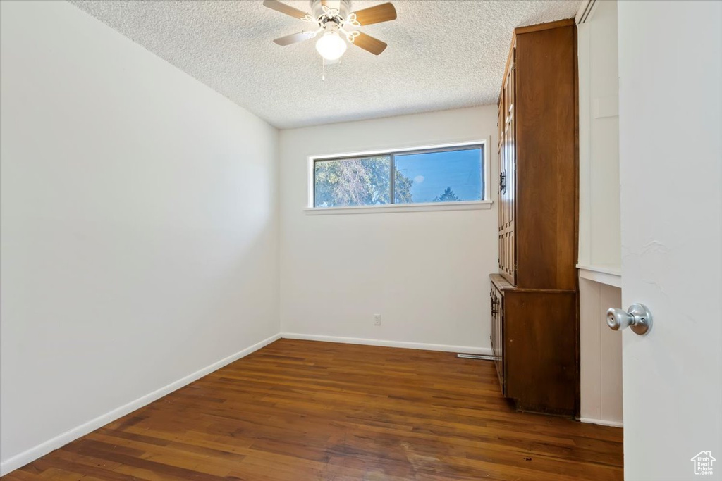 Empty room with a ceiling fan, a textured ceiling, and dark wood-type flooring