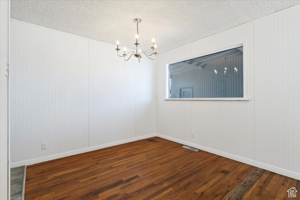 Spare room featuring a chandelier, wood finished floors, and a textured ceiling
