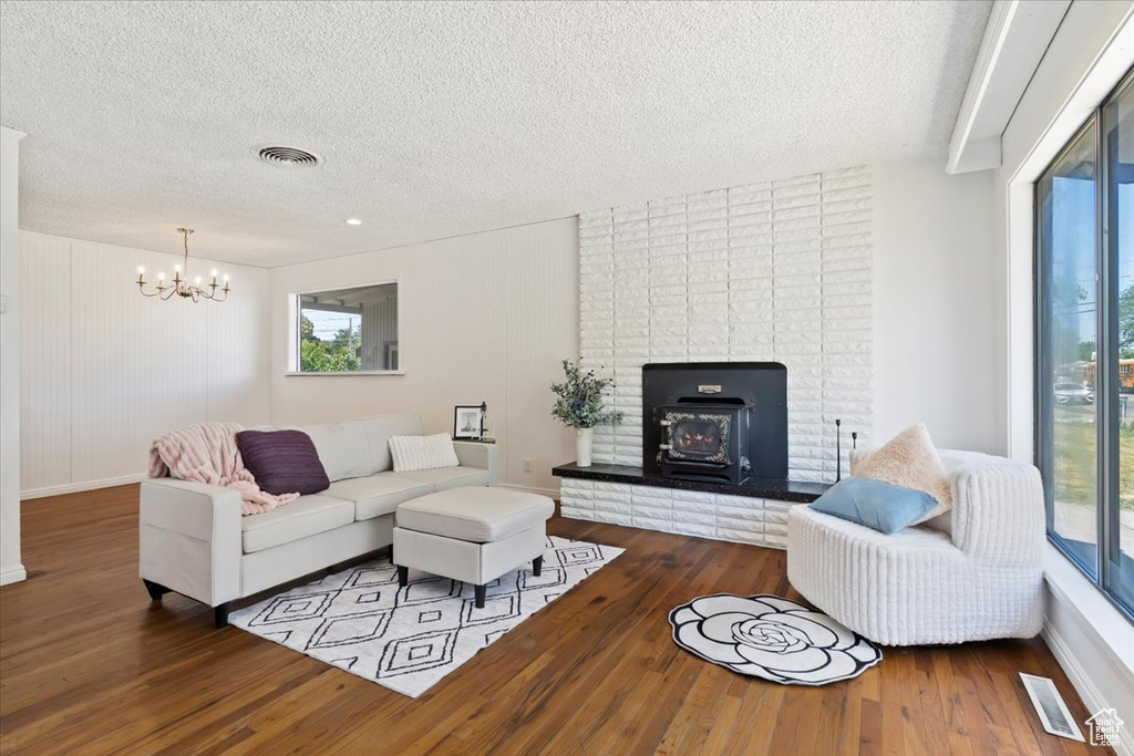 Living room with a textured ceiling, wood finished floors, a wood stove, and a chandelier