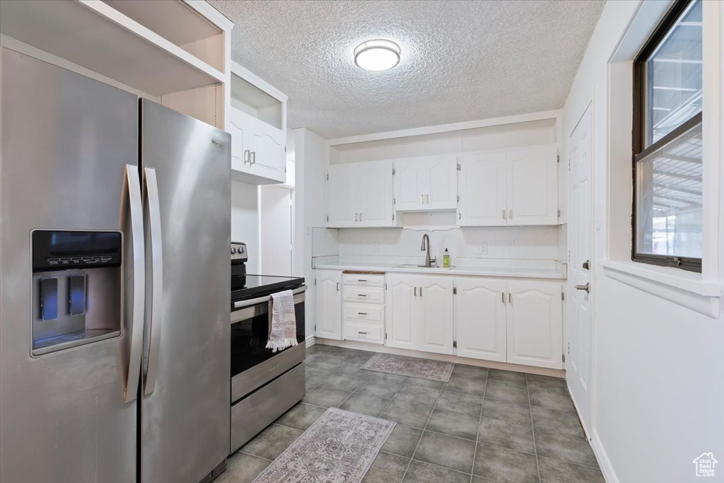 Kitchen featuring appliances with stainless steel finishes, a textured ceiling, white cabinets, light countertops, and open shelves