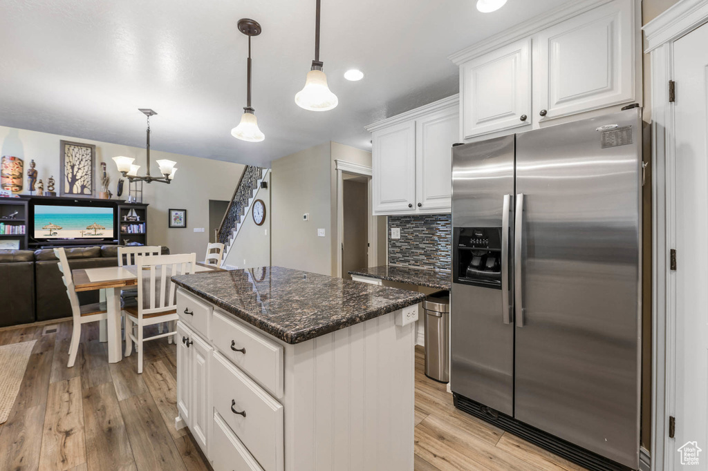 Kitchen with stainless steel fridge, a center island, backsplash, a chandelier, and white cabinets