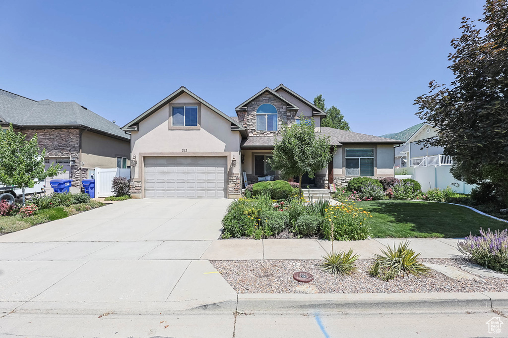 View of front facade with stucco siding, driveway, an attached garage, and stone siding