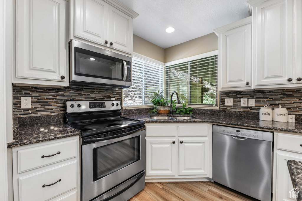 Kitchen with stainless steel appliances, white cabinetry, decorative backsplash, and light wood-type flooring