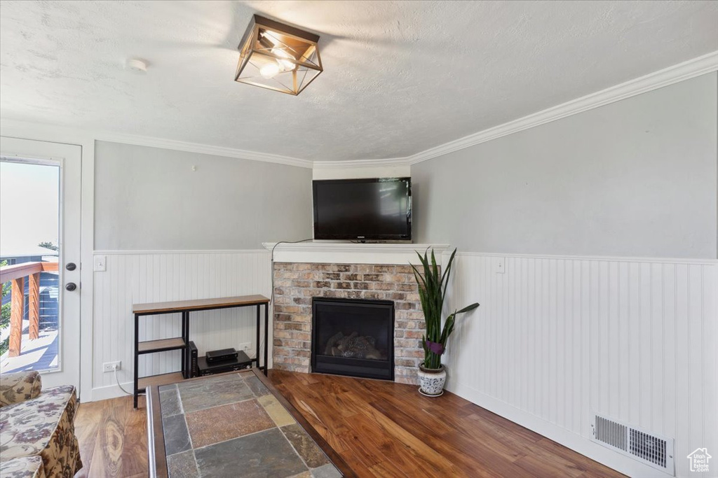 Living area with wood finished floors, wainscoting, a fireplace, crown molding, and a textured ceiling