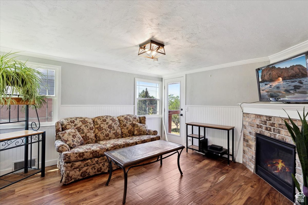 Living room with plenty of natural light, a wainscoted wall, wood finished floors, a brick fireplace, and crown molding