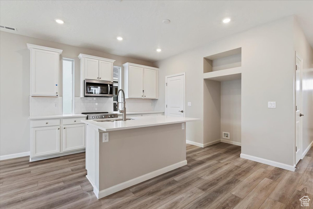 Kitchen with stainless steel microwave, light wood-style flooring, a kitchen island with sink, decorative backsplash, and recessed lighting