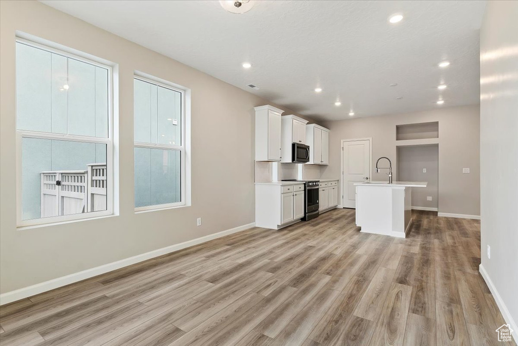Kitchen with stainless steel appliances, light wood finished floors, an island with sink, white cabinets, and recessed lighting
