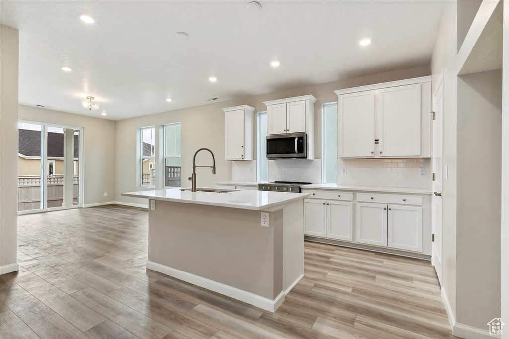 Kitchen with stainless steel microwave, a kitchen island with sink, light wood-style floors, tasteful backsplash, and recessed lighting