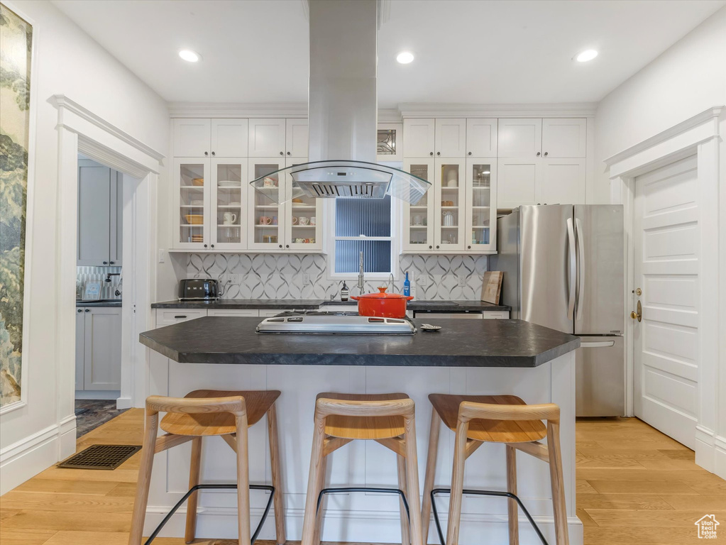 Kitchen featuring freestanding refrigerator, island range hood, dark countertops, decorative backsplash, and white cabinets