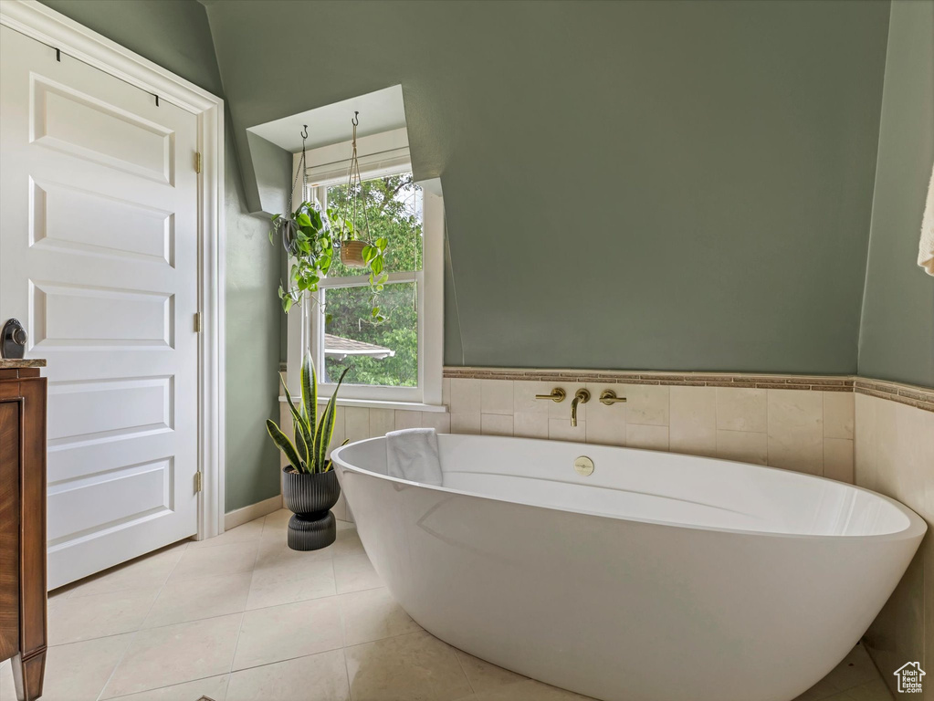 Bathroom with a freestanding bath, a wainscoted wall, plenty of natural light, tile patterned floors, and tile walls