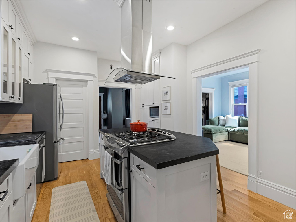 Kitchen featuring appliances with stainless steel finishes, dark countertops, exhaust hood, glass insert cabinets, and white cabinets