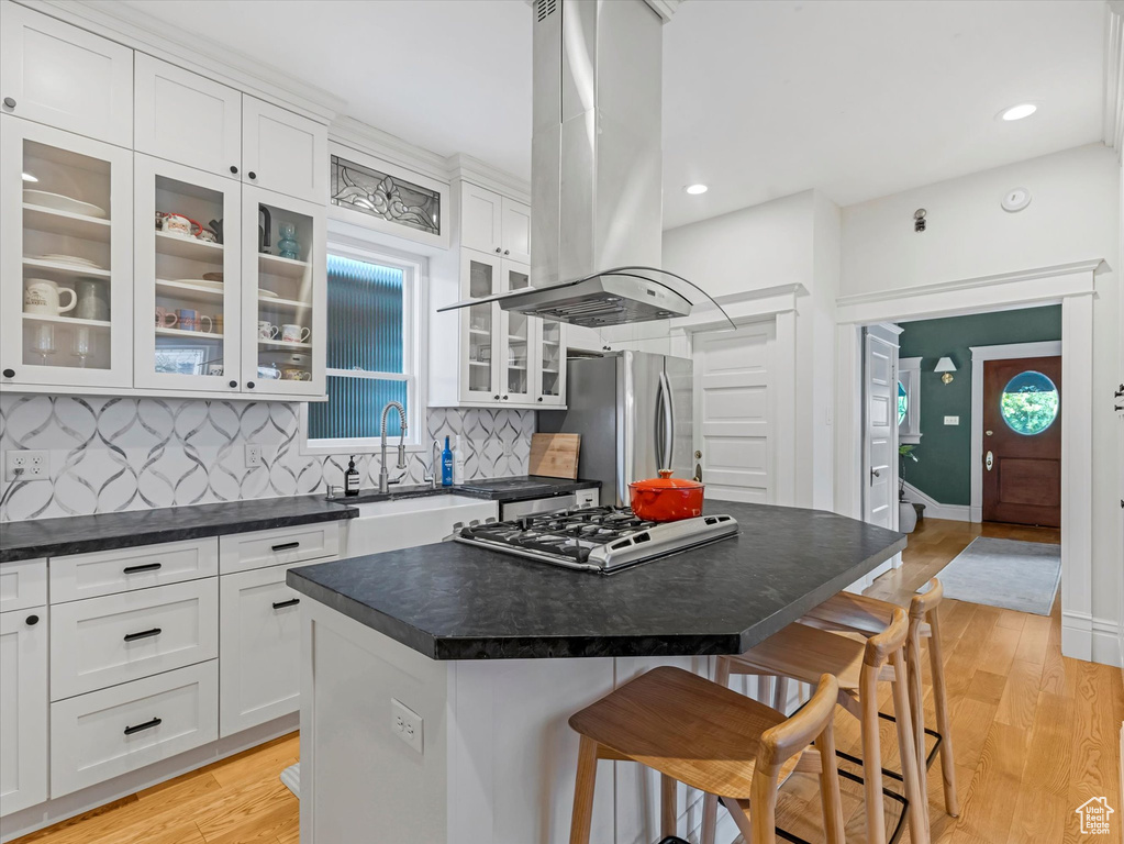 Kitchen featuring freestanding refrigerator, island range hood, a breakfast bar area, dark countertops, and white cabinetry