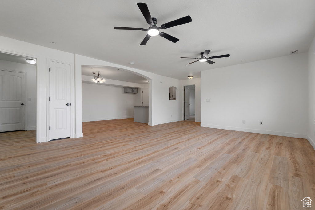 Unfurnished living room featuring ceiling fan, light wood-style floors, arched walkways, a wall mounted AC, and a chandelier