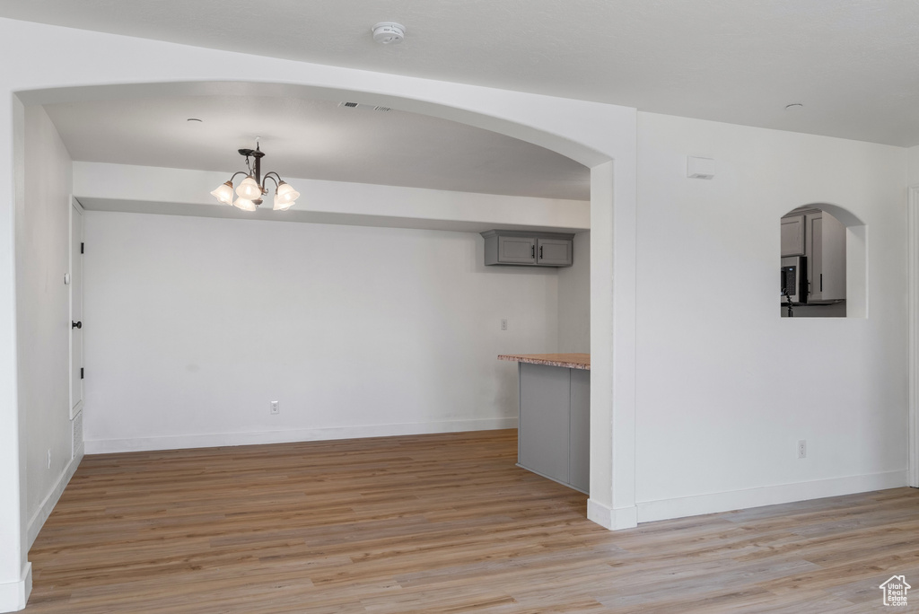Unfurnished dining area featuring light wood-style flooring, a chandelier, and arched walkways