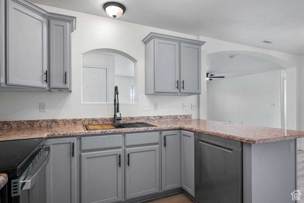 Kitchen with appliances with stainless steel finishes, gray cabinetry, a peninsula, and arched walkways