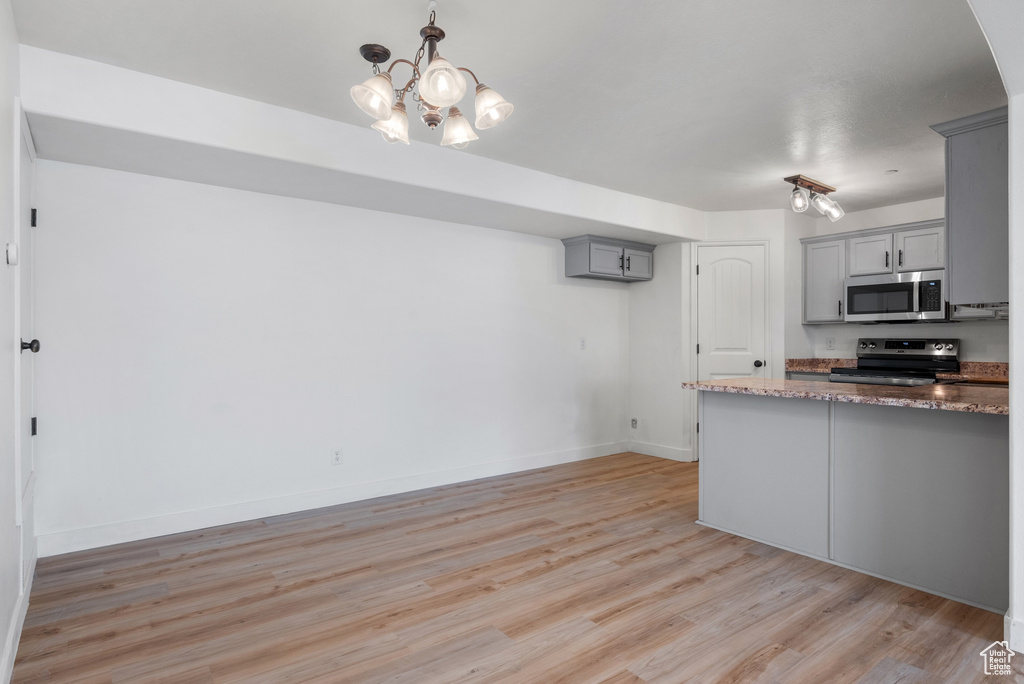 Kitchen featuring stainless steel appliances, gray cabinetry, light wood-style floors, stone counters, and a chandelier