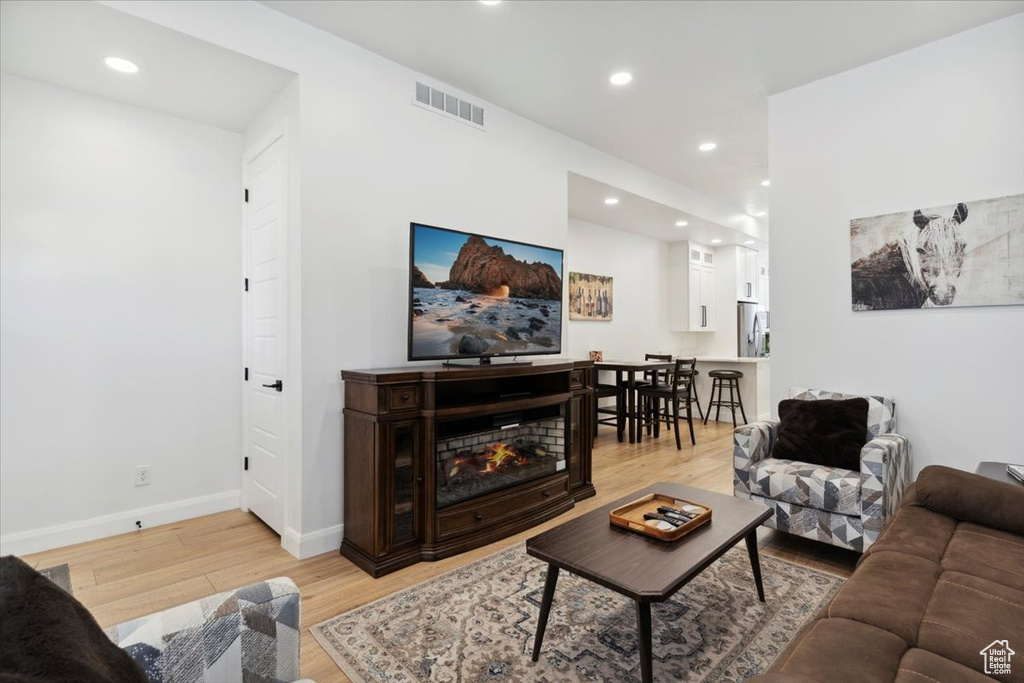 Living room with light wood finished floors, recessed lighting, and a glass covered fireplace