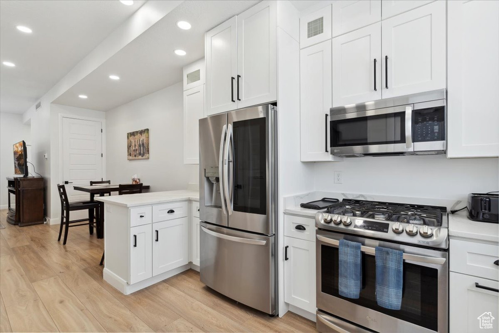 Kitchen featuring stainless steel appliances, recessed lighting, a peninsula, light countertops, and white cabinetry