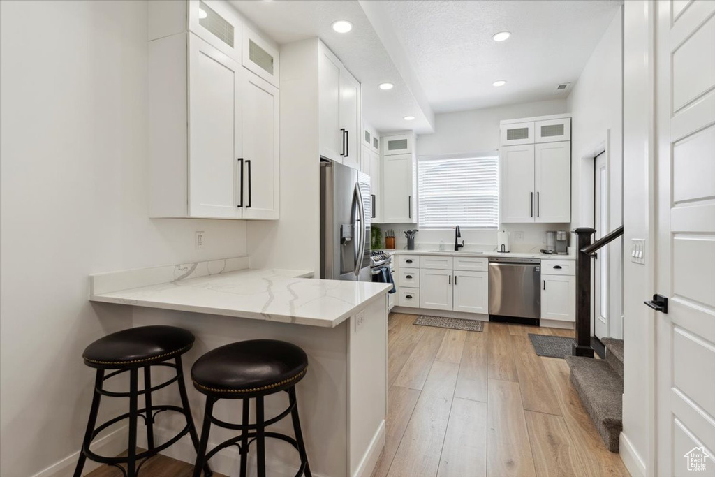 Kitchen featuring appliances with stainless steel finishes, a breakfast bar, a peninsula, white cabinets, and recessed lighting