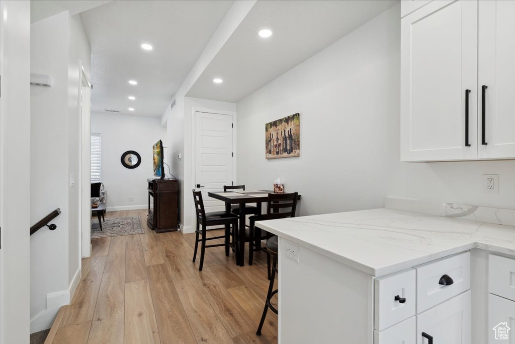 Kitchen with light wood-type flooring, recessed lighting, white cabinets, light stone counters, and a kitchen breakfast bar