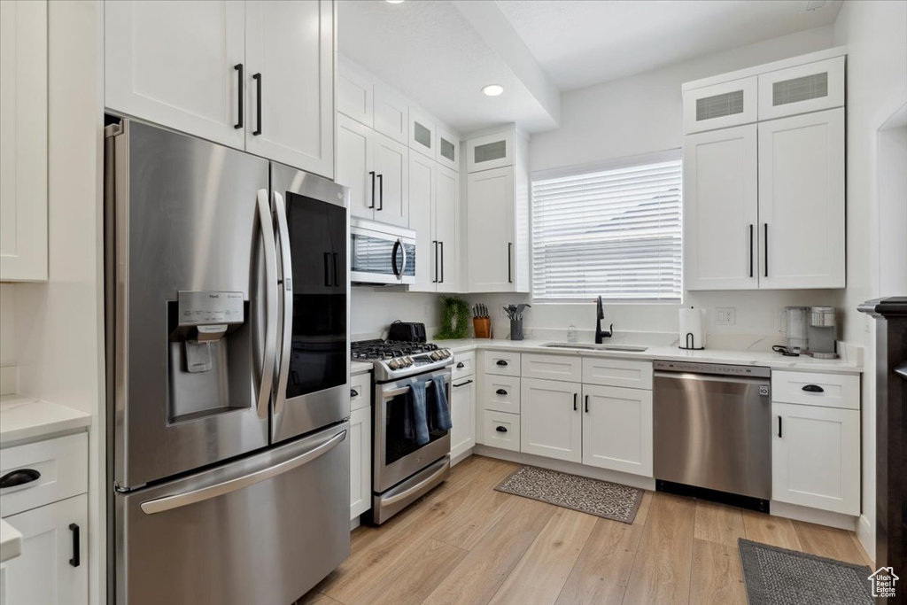 Kitchen with stainless steel appliances, white cabinetry, recessed lighting, glass insert cabinets, and light wood finished floors